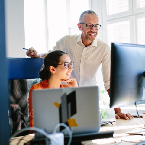 Frau und Mann blicken lächelnd auf Bildschirmmonitor