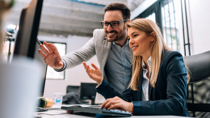Mann und Frau zeigen lächelnd auf einen Computermonitor