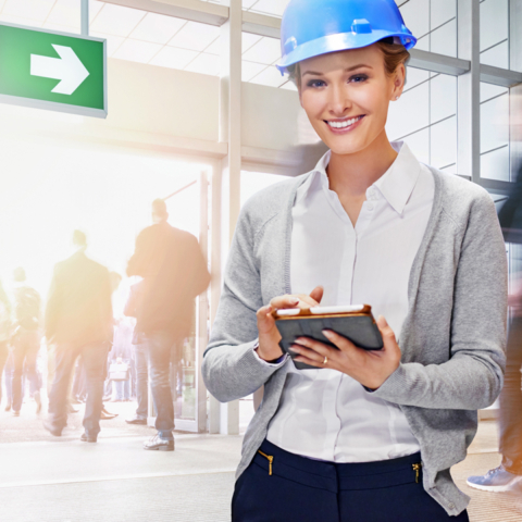 Lächelnde Frau mit Schutzhelm und Tablet in der Hand während einer Evakuierung eines Gebäudes