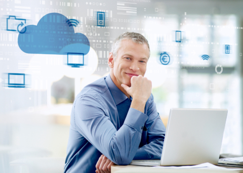 Mann sitzt lächelnd am Schreibtisch mit Laptop