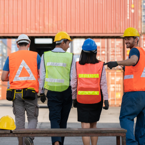 Eine Gruppe von Personen mit Schutzhelmen geht im Gespräch auf einen Gebäudeeingang zu