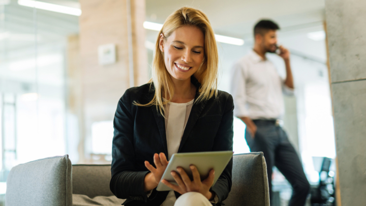 Frau im Sessel im modernen Büro blickt lächelnd auf ein Tablet