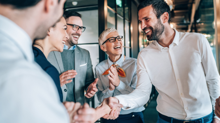 Gruppe von lachenden Menschen, zwei Personen geben sich die Hand