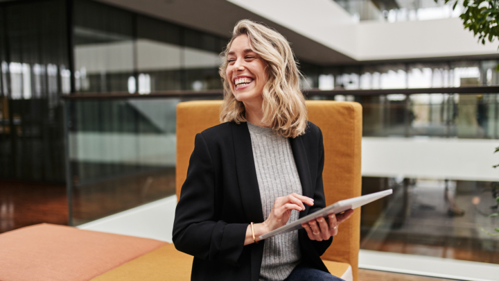 Femme dans un immeuble de bureaux moderne, tenant une tablette et souriant