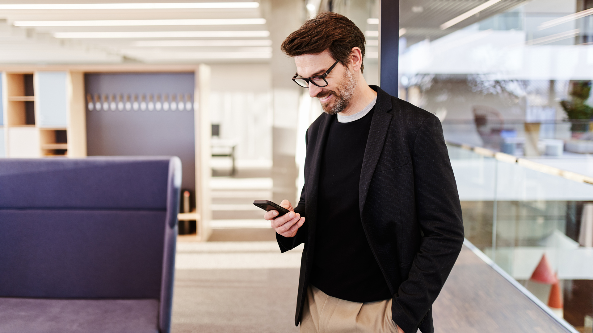 Un homme dans un bâtiment d'entreprise moderne, souriant en regardant l'écran de son smartphone