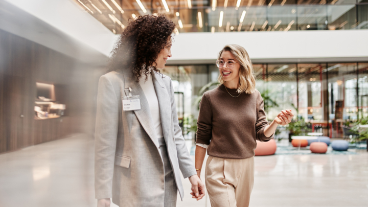 Deux femmes discutent et sourient en marchant dans un immeuble de bureaux