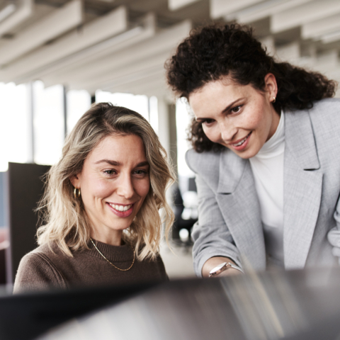 Zwei Frauen blicken lächelnd auf einen Bildschirmmonitor